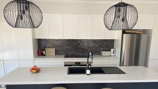 A modern kitchen with white cabinets, a black backsplash, stainless steel appliances, and two wooden stools. - Modern, comfort and serenity in Fitzroy Falls (Fitzroy Falls)