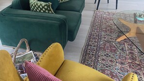 A living room with a green sofa, a yellow armchair, a patterned rug, and a wooden cabinet with decorative items. - Modern, comfort and serenity in Fitzroy Falls (Fitzroy Falls)