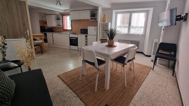 Een moderne keuken met witte kasten, een eethoek met een tafel en stoelen, en een aan de muur bevestigde televisie.