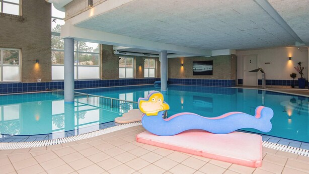 An indoor swimming pool with a lifeguard stand, tiled walls, and a large window.