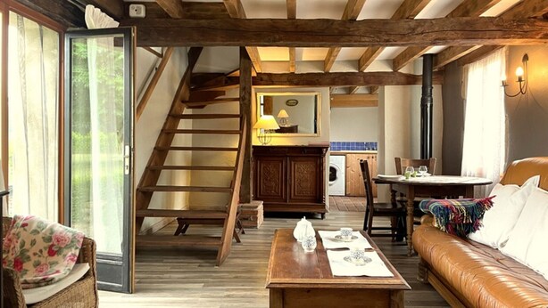 A rustic interior with exposed wooden beams, a staircase, a dining area, and a cozy seating space. - Charming cottage in Lurcy-Lévis with air conditioning and garden (Lurcy-Lévis)