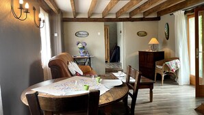 A dining area with a wooden table and chairs, a vase of flowers, and a lamp on a side table. - Charming cottage in Lurcy-Lévis with air conditioning and garden (Lurcy-Lévis)