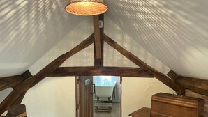 An attic room with exposed wooden beams, a woven light fixture, and a wooden chest of drawers. - Charming cottage in Lurcy-Lévis with air conditioning and garden (Lurcy-Lévis)