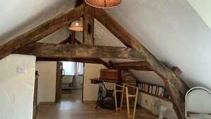 A loft bedroom with exposed wooden beams, a wooden desk, a sewing machine, and a fan. - Charming cottage in Lurcy-Lévis with air conditioning and garden (Lurcy-Lévis)