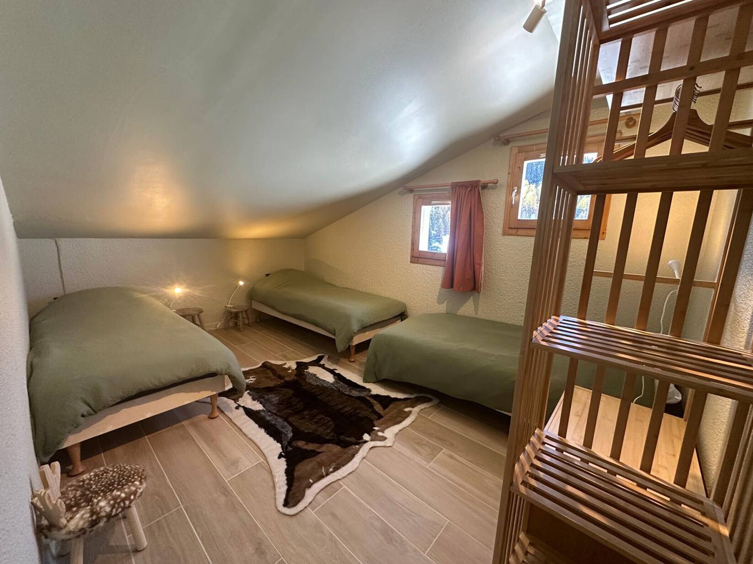 Une petite chambre mansardée, chaleureuse et accueillante, avec deux lits, un berceau en bois et un tapis rustique.