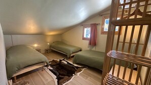 Ein kleines, gemütliches Schlafzimmer im Dachgeschoss mit zwei Betten, einem Holckrippen und einem rustikalen Teppich.