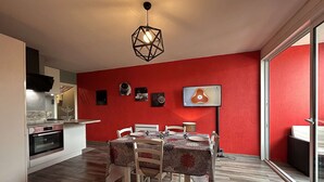 Une cuisine moderne dotée d’un four encastré, un coin repas avec une table et des chaises, et un mur d’accent de couleur rouge.