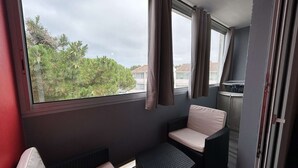 Un balcon avec des meubles en osier, une vue sur les arbres et les bâtiments, et une fenêtre avec des rideaux.