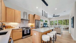 A modern kitchen with wooden cabinets, a central island with bar stools, a built-in oven, and a stainless steel refrigerator.