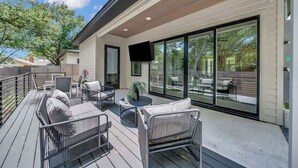 A modern outdoor deck with seating, a flat-screen TV, and large sliding glass doors.