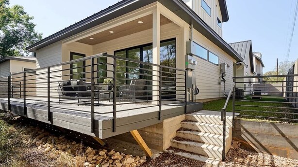 A modern house with a covered patio, outdoor seating, and a visible staircase leading to the entrance.