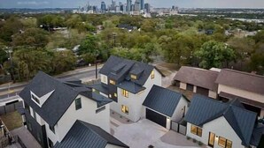 A residential area with modern houses, a city skyline in the background, and a clear sky. - Great Deal, 6bd, Pool,  Game Room & Chef Kitchen (Austin)