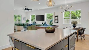 A modern kitchen with a central island, pendant lighting, and a dining area with a table and chairs. - Great Deal, 6bd, Pool,  Game Room & Chef Kitchen (Austin)