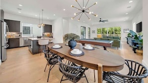 A modern kitchen with a dining area, featuring a central island, dark cabinetry, and a contemporary light fixture. - Great Deal, 6bd, Pool,  Game Room & Chef Kitchen (Austin)