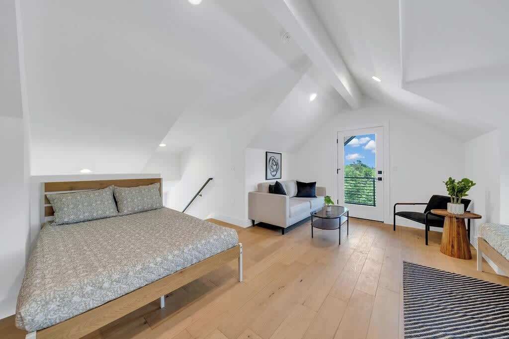 Ein modernes Schlafzimmer im Loft-Stil mit einem großen Bett, einer Couch, einem kleinen Tisch und Blick ins Freie.