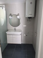 Un baño con un lavabo blanco, un espejo redondo y un calentador en la pared.