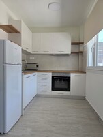 Una cocina compacta con armarios blancos, horno integrado y refrigerador.