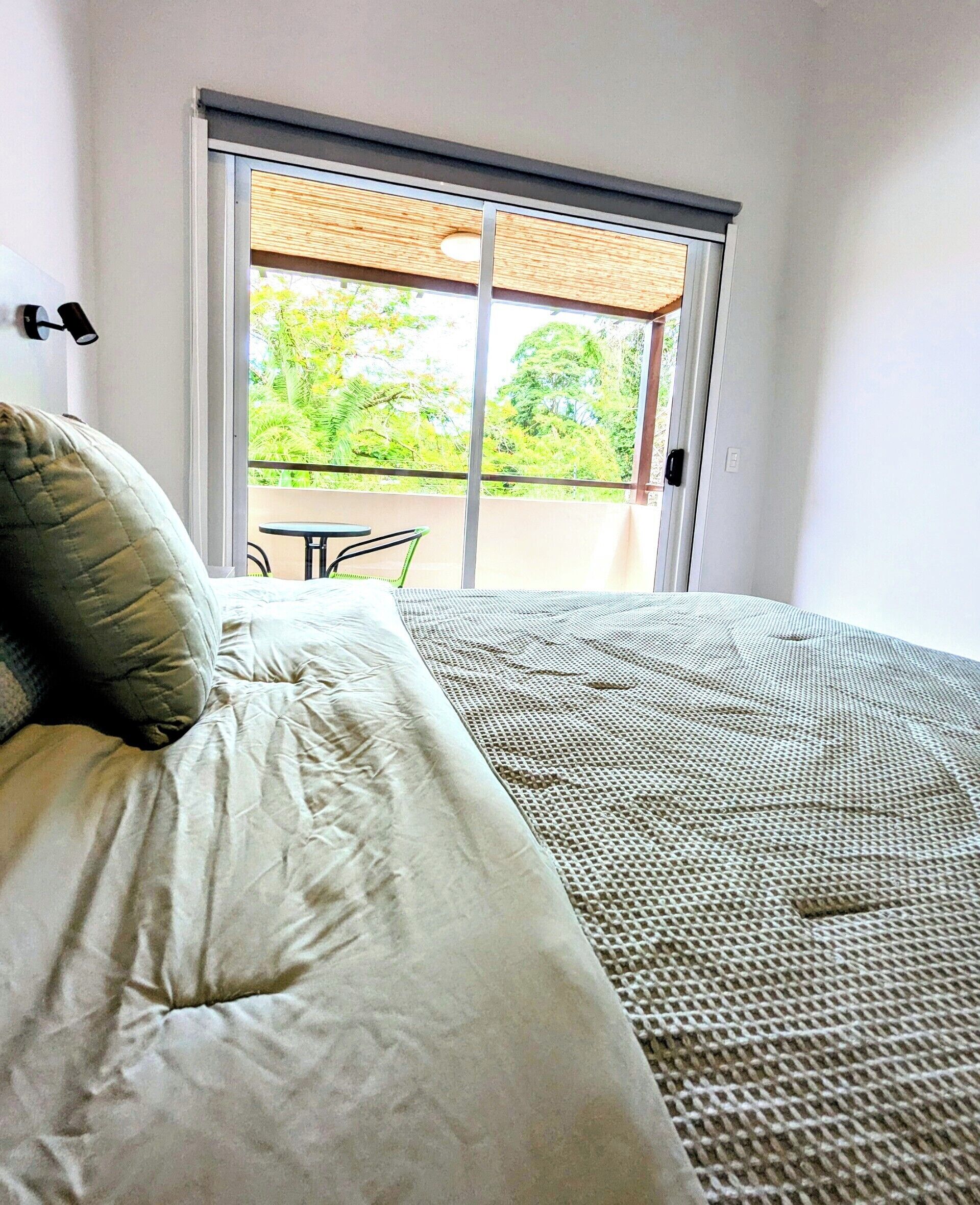 A bedroom with a bed, a view of a balcony, and a door leading outside.