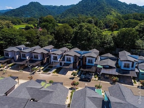 A residential area with modern houses, a clear road, and a hilly landscape in the background. - Upscale Tropical Retreat | 4BR in Gated Resort (Jaco)
