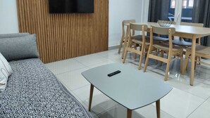 Ein modernes Wohnzimmer mit einer Couch, einem Couchtisch, einem Esstisch mit Stühlen und einem Flachbildfernseher, der an einer Holzwand angebracht ist.
