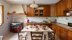 A kitchen with wooden cabinets, a gas stove, a dining table set with chairs, and a hanging light fixture.