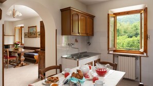 A dining area with a table set for breakfast, a kitchen with wooden cabinets, and a window with a view of greenery.
