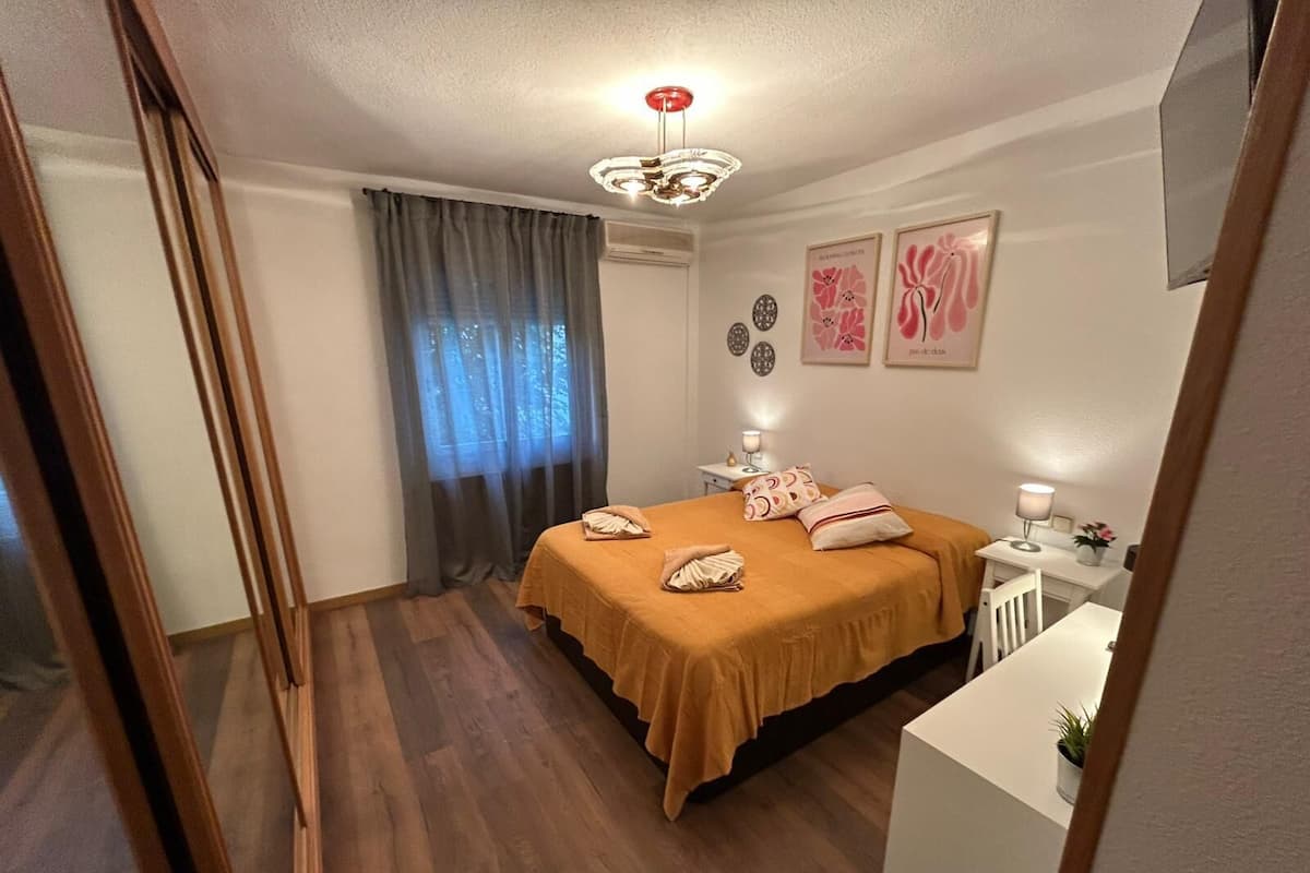 Un dormitorio con cama, mesita de noche con lámpara, ventana con cortinas y decoración en la pared.