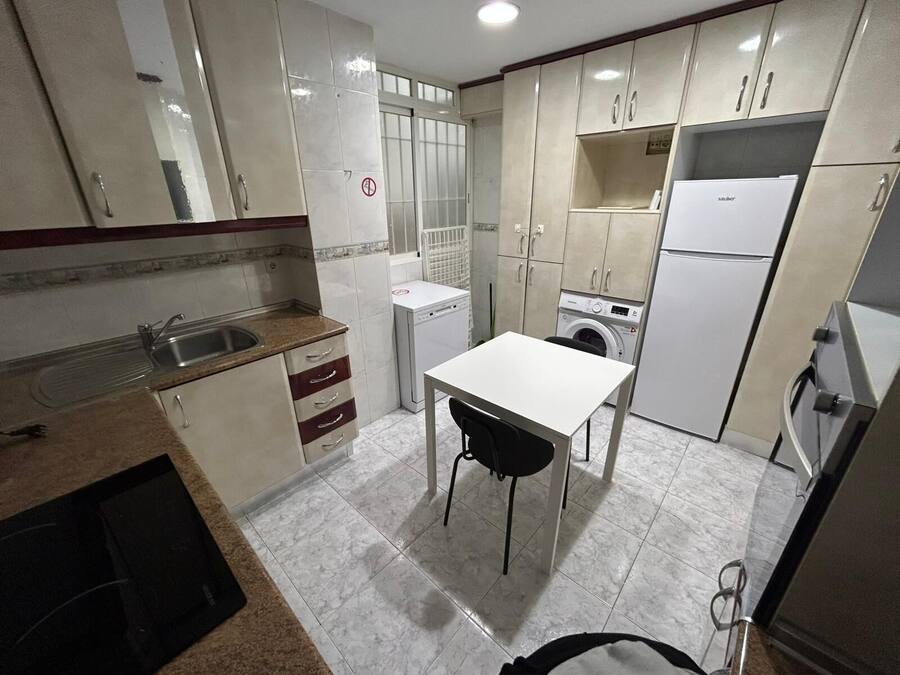 A compact kitchen with a sink, a dishwasher, a washing machine, and a refrigerator.