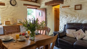 Un intérieur rustique avec une table à manger en bois, préparée pour le petit-déjeuner, un canapé en cuir et un mur en pierre.