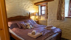Une chambre à coucher chaleureuse avec un lit en bois, une literie à rayures, un ours en peluche et une fenêtre ornée de rideaux à motifs floraux.