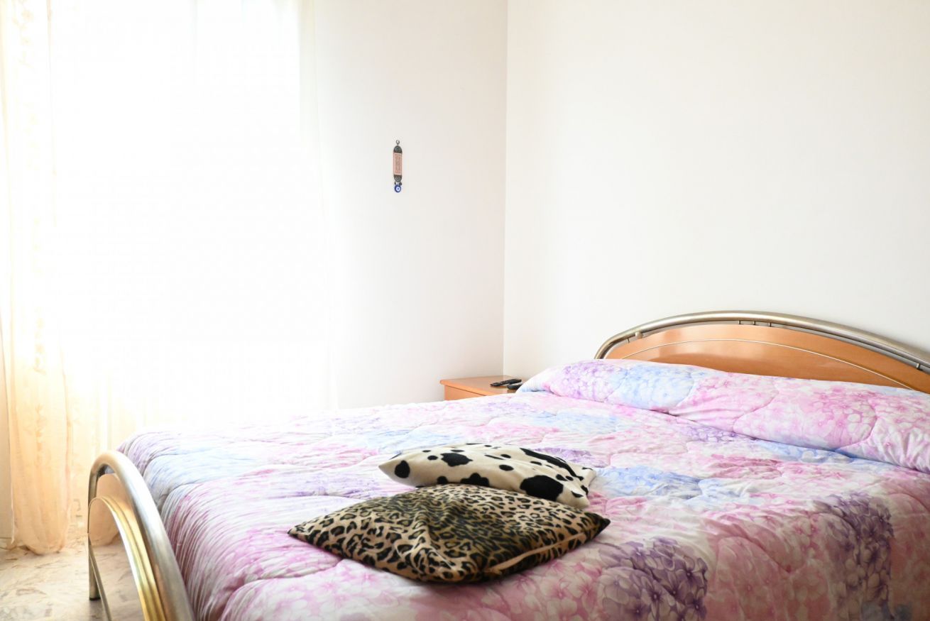 A bedroom with a bed, two pillows, a nightstand, and a wall-mounted light.