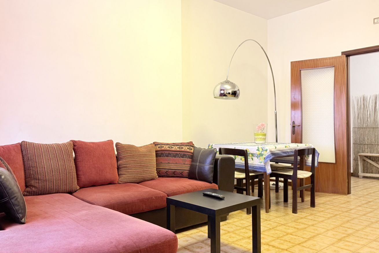 A living room with a sofa, a dining table with chairs, a lamp, and a door.