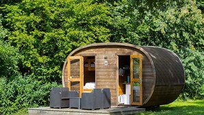 Een houten cilindervormige accommodatie met een terras, twee deuren en een klein zitgedeelte.