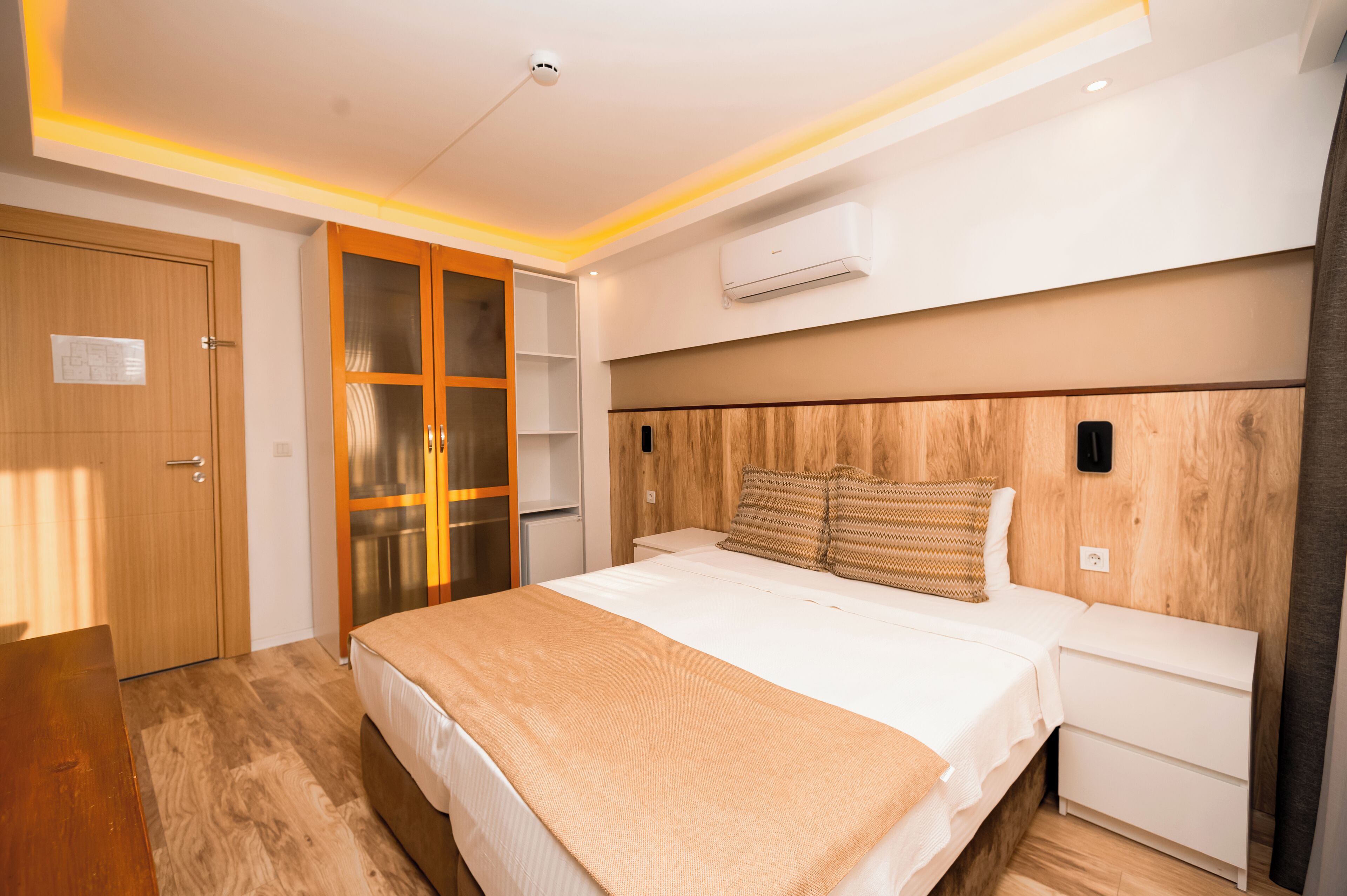 Un dormitorio moderno con cama, mesitas de noche, un armario y un equipo de aire acondicionado.