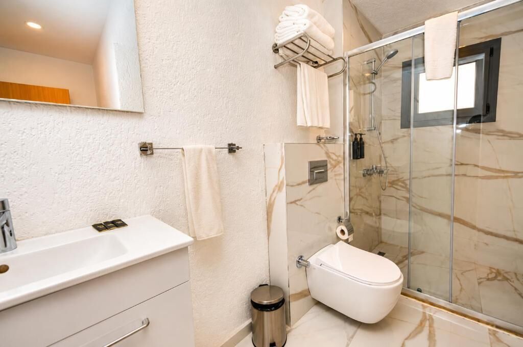 Un baño con ducha de mármol, inodoro, lavabo y espejo.