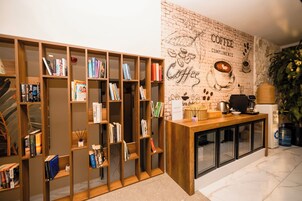 Un rincón acogedor para leer con estanterías de madera llenas de libros y una estación de café con cafetera y una cesta.