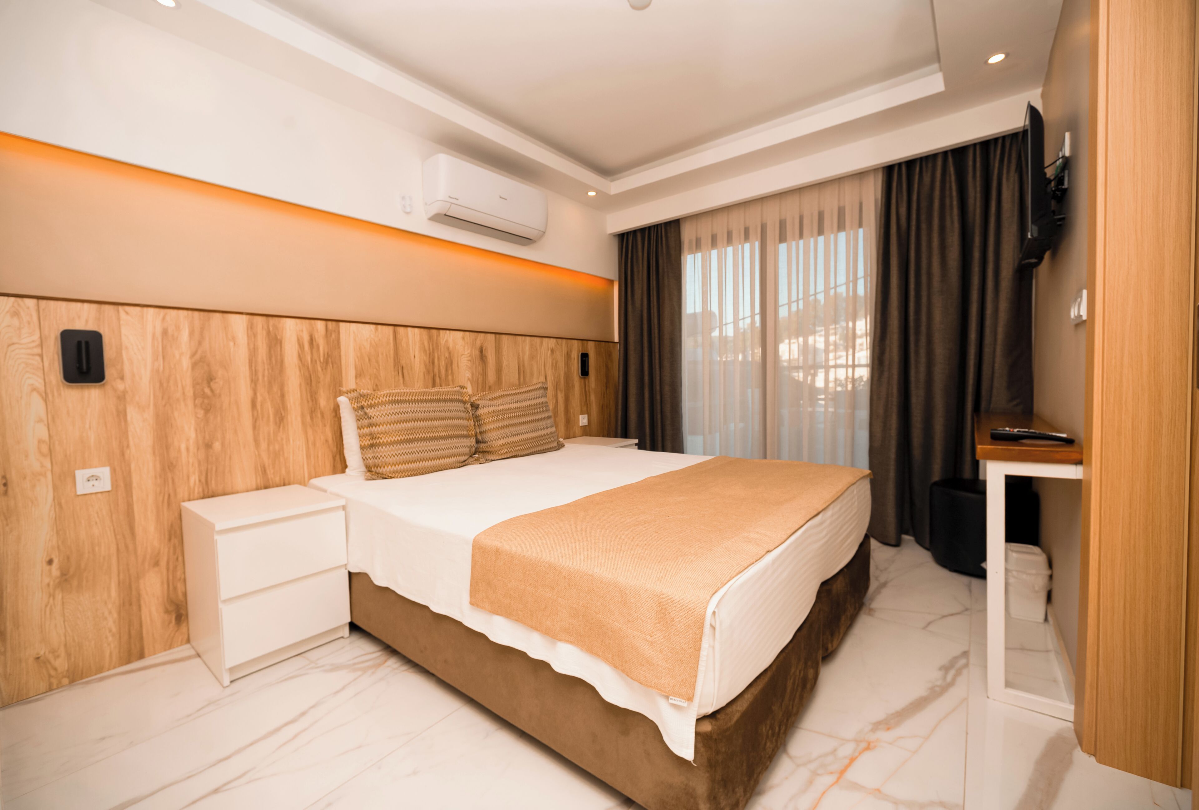 A modern hotel room with a large bed, a bedside table, an air conditioning unit, and a television.