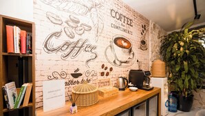A coffee-themed wall with a brick pattern, a wooden counter with a coffee machine, books, and a sign that reads "Coffee is complimentary."