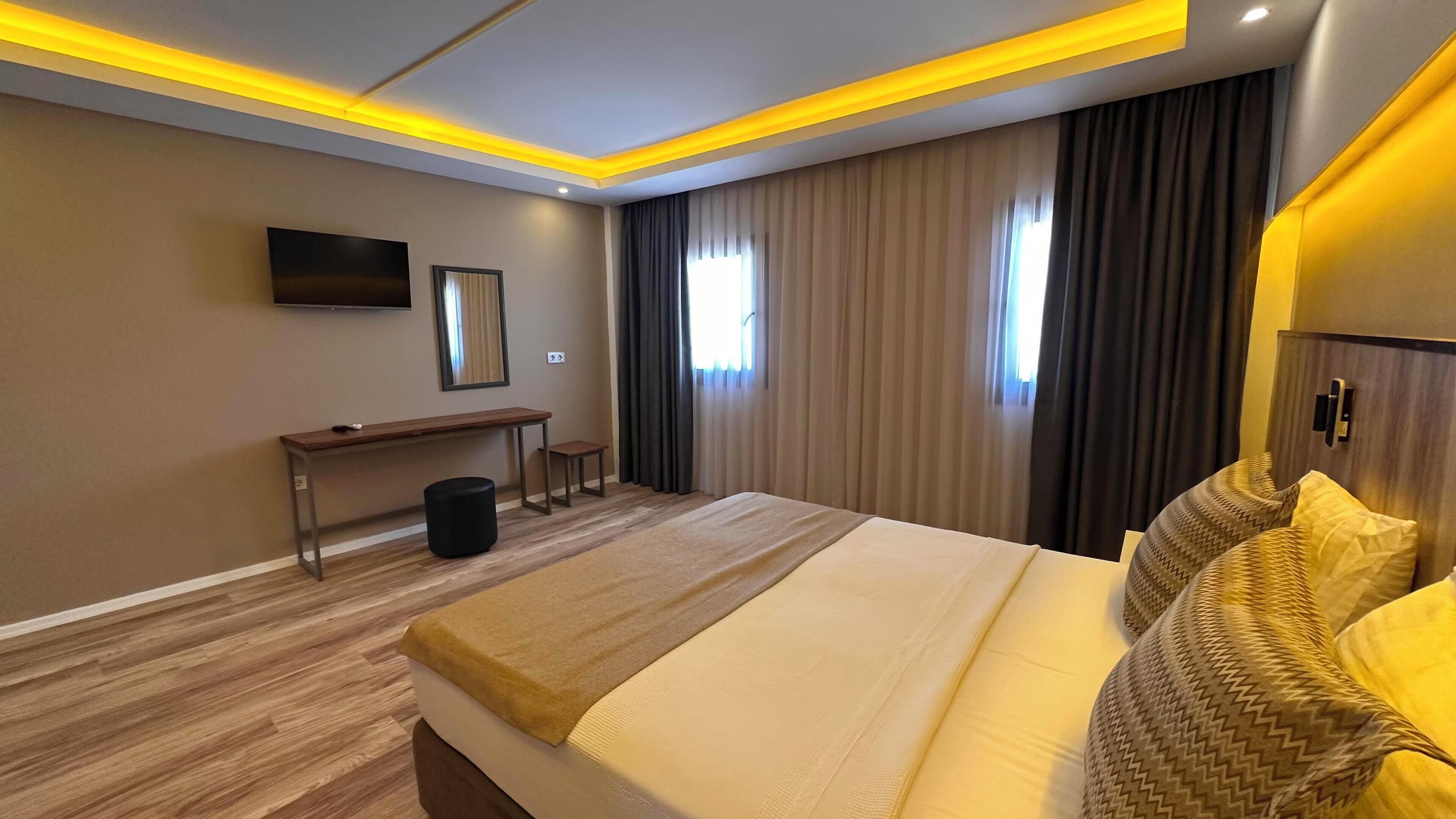 Ein Hotelzimmer mit einem Bett, einem Schreibtisch, einem Stuhl, einem kleinen Hocker und einem an der Wand montierten Fernseher.
