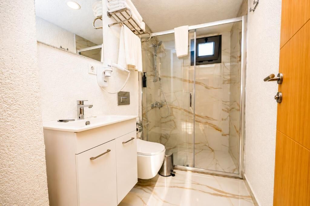 A bathroom with a white vanity, a toilet, a glass shower enclosure, and a wooden door.