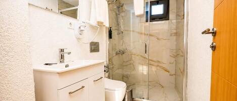 A bathroom with a white vanity, a toilet, a glass shower enclosure, and a wooden door.