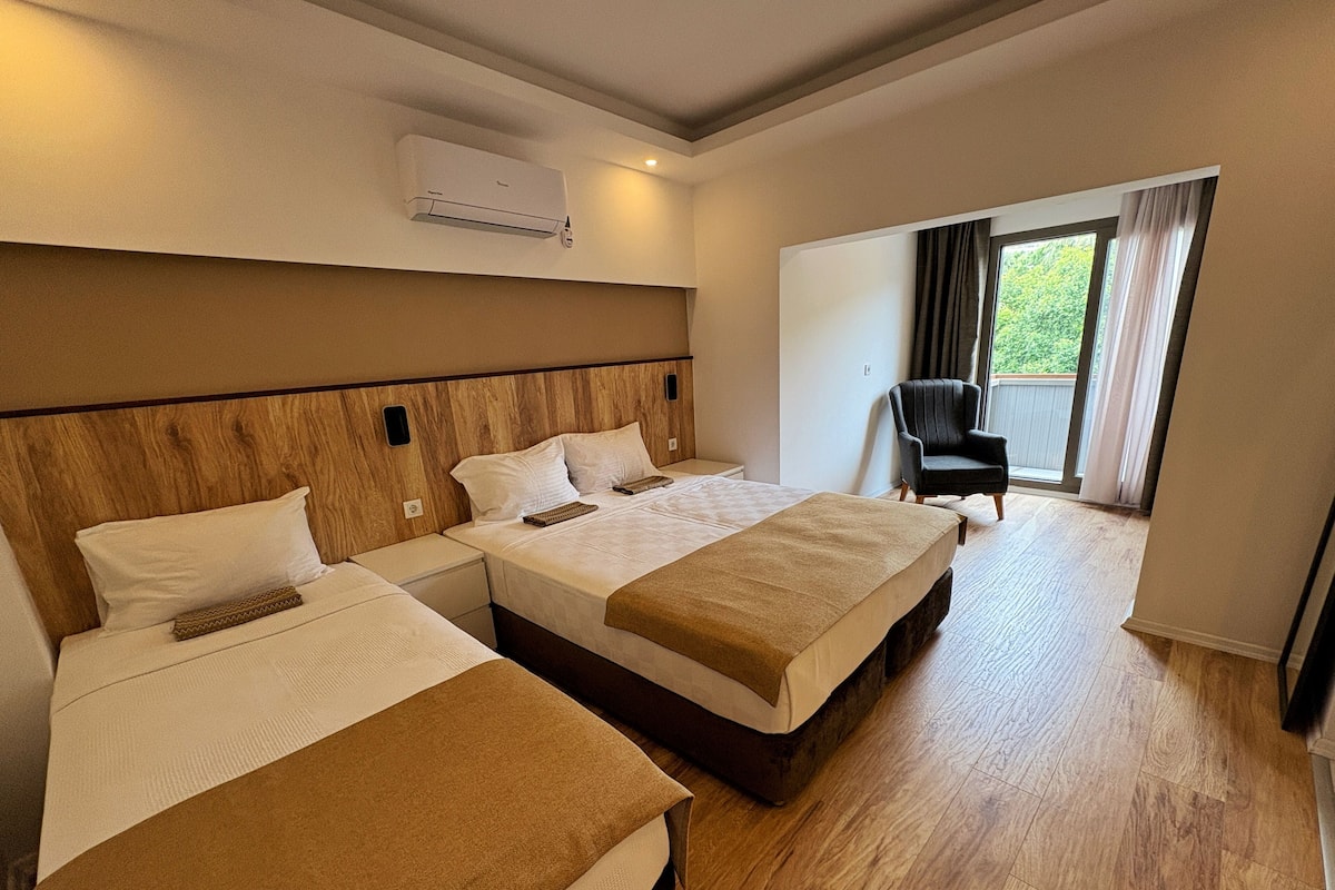 A hotel room with two beds, a wooden headboard, a large window with curtains, and an air conditioning unit.