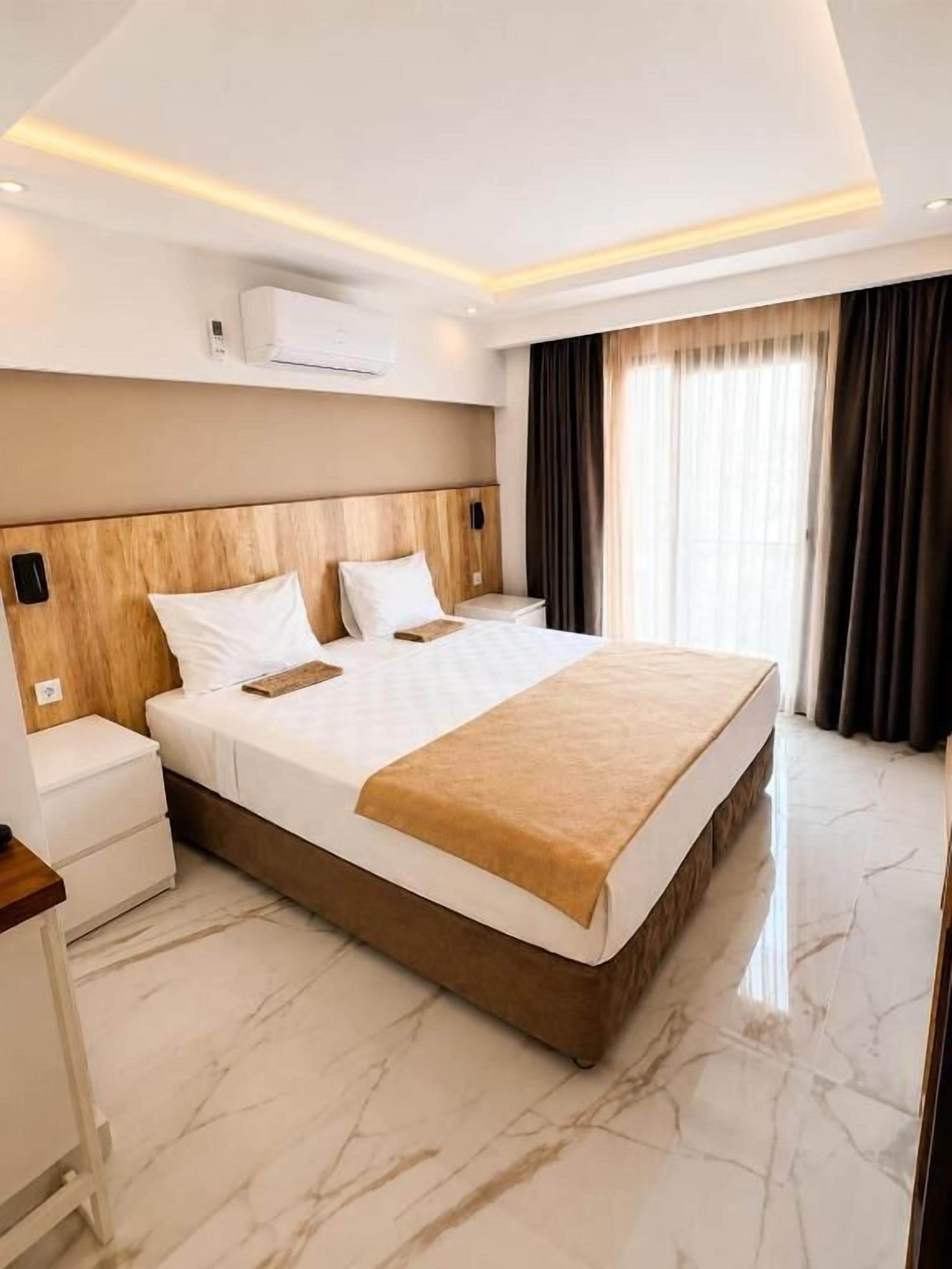Une chambre d’hôtel avec un grand lit, une table de chevet, un appareil de climatisation et une fenêtre avec des rideaux.