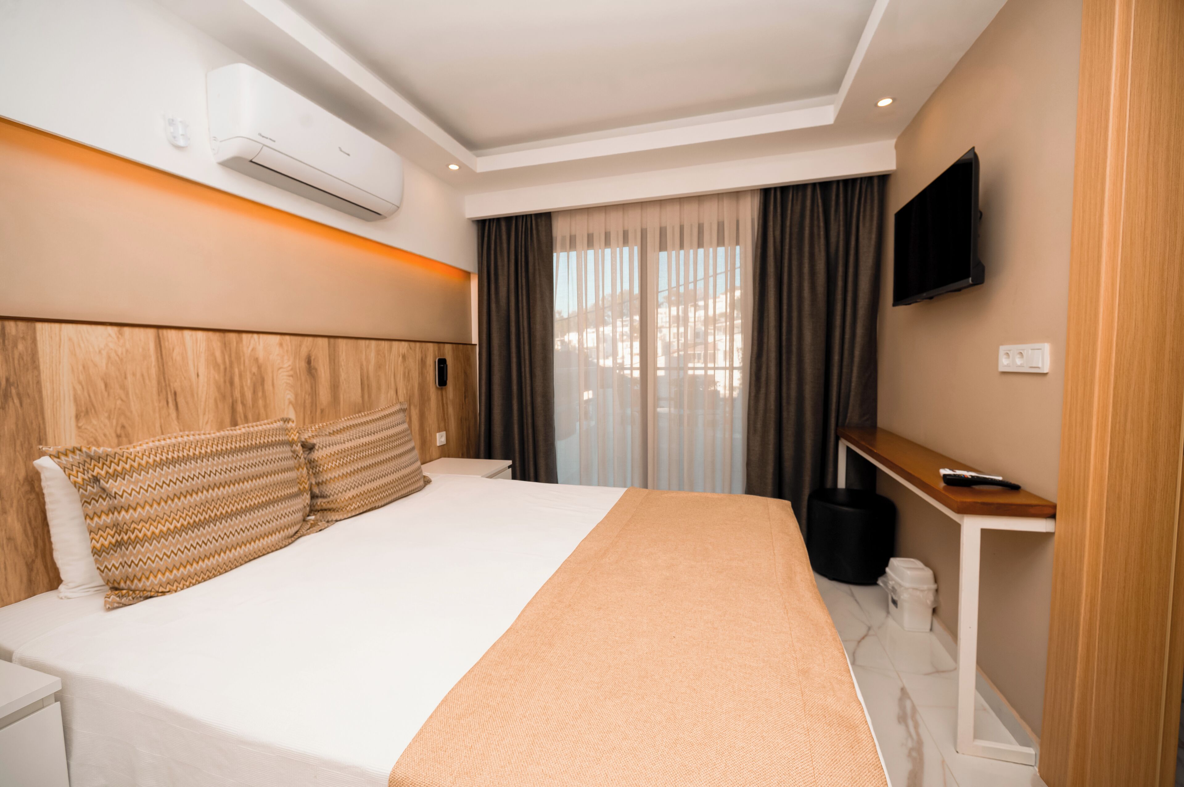 A modern hotel room with a large bed, a bedside table, a TV, and an air conditioning unit.