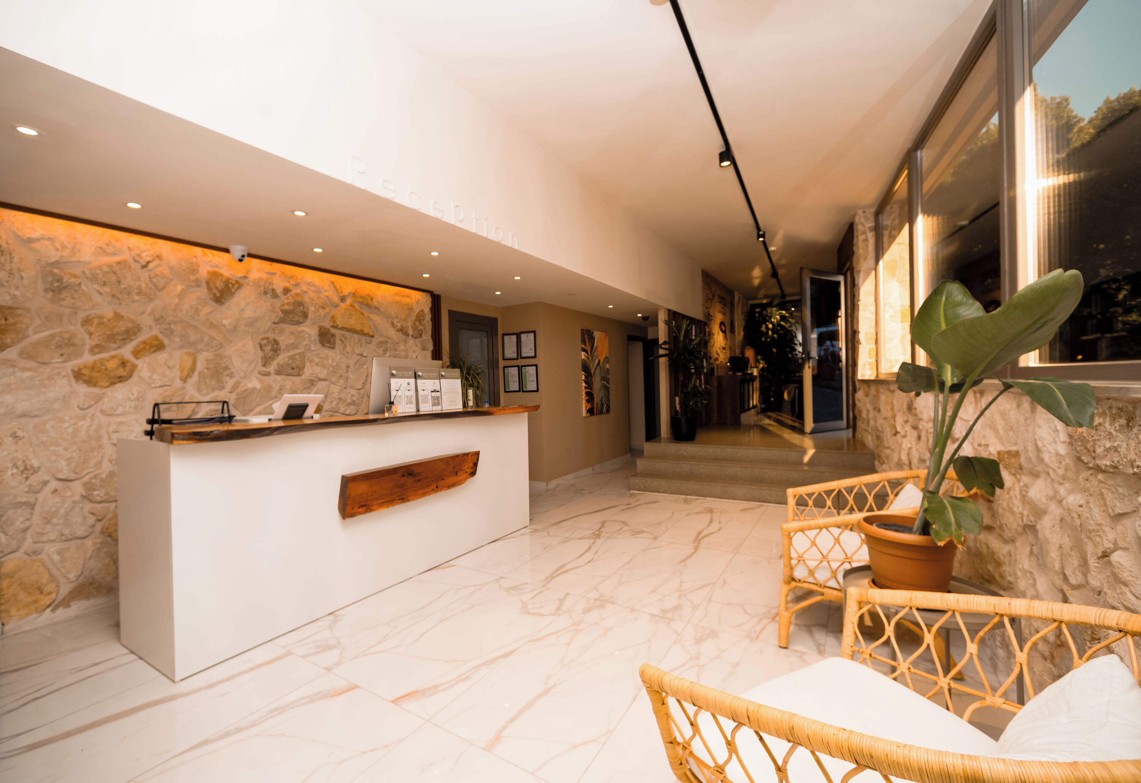 A reception area with a stone wall, a reception desk, wicker chairs, and a potted plant.