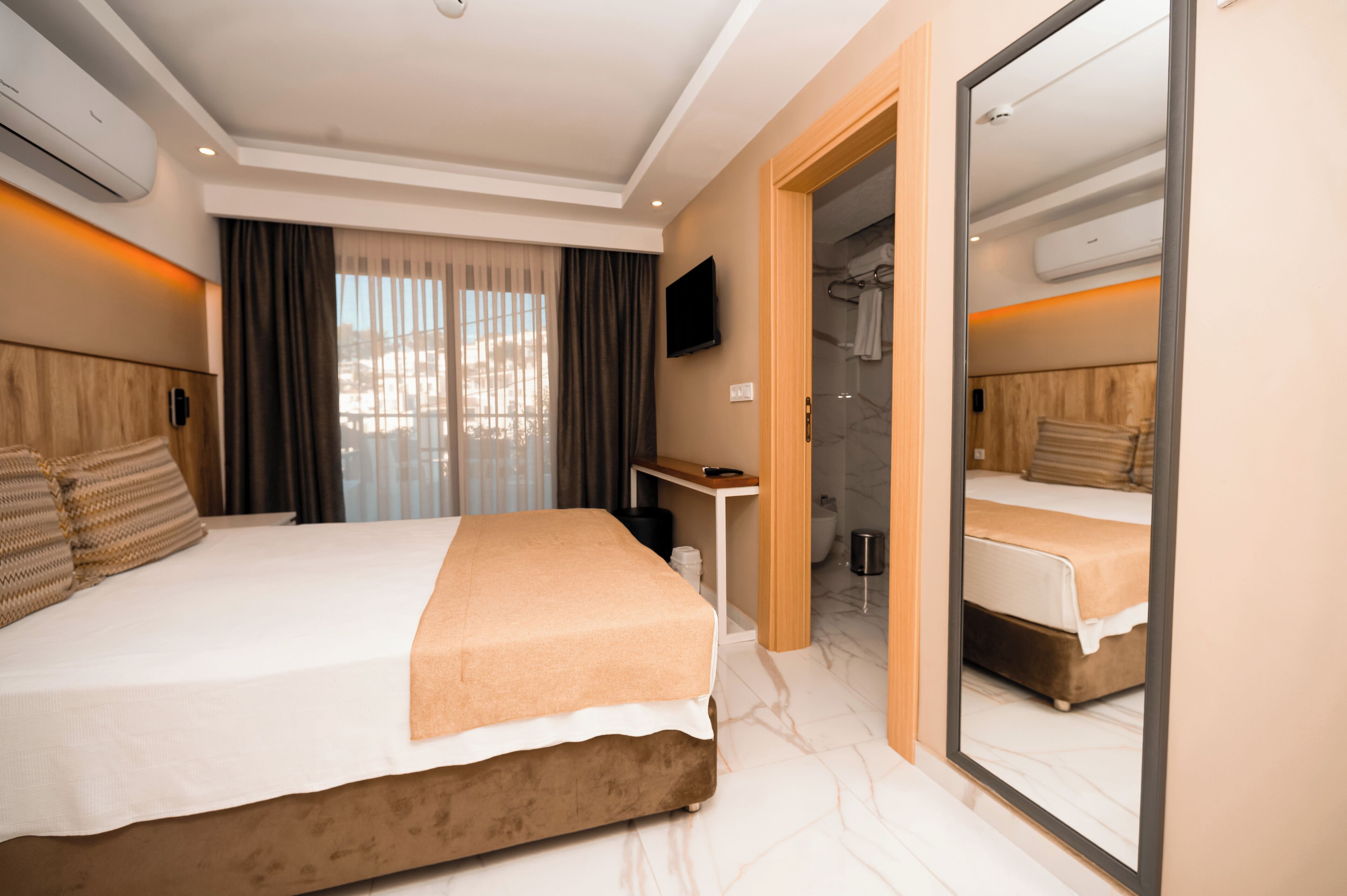 Ein modernes Hotelzimmer mit einem großen Bett, einem Schreibtisch, einem Spiegel und einem durch eine offene Tür einsehbaren Badezimmer.