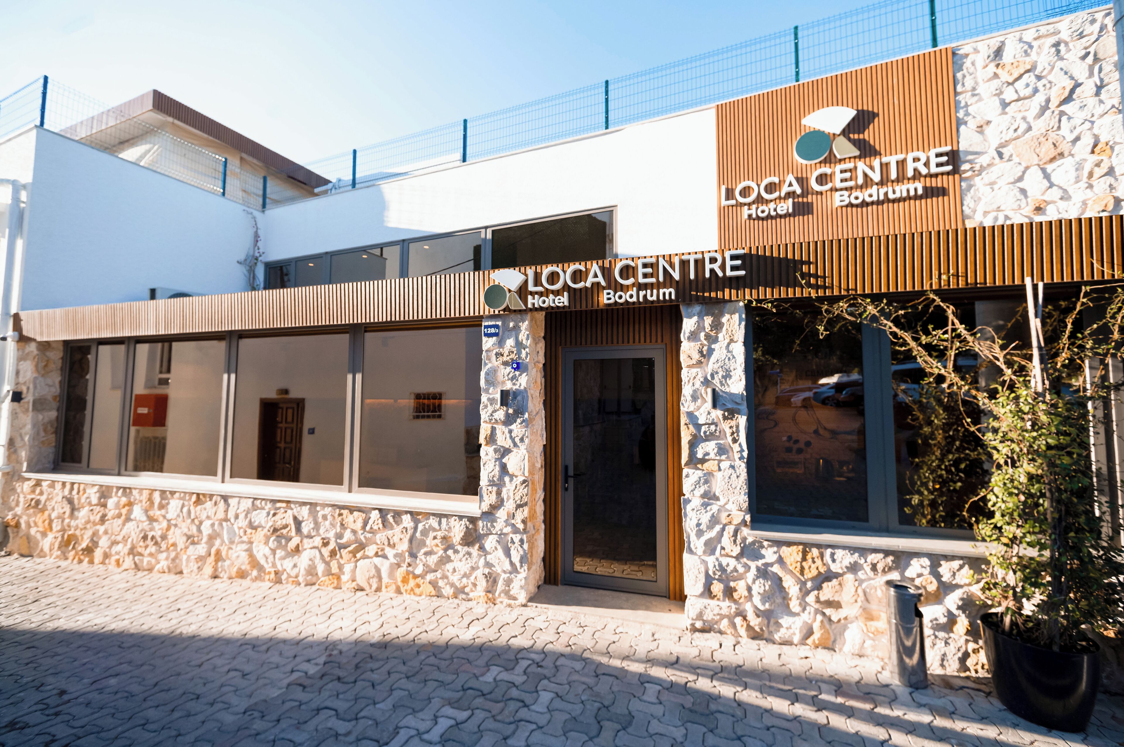 Fachada de hotel con revestimiento de piedra, sección superior de madera y un letrero que dice 'LOCA CENTRE Bodrum Hotel'.