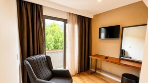 A room with a chair, a desk, a TV, and a window with curtains.