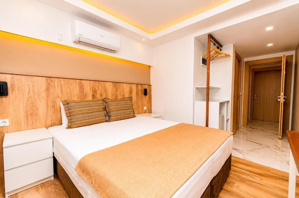 A hotel room with a bed, bedside table, wardrobe, and an air conditioning unit.