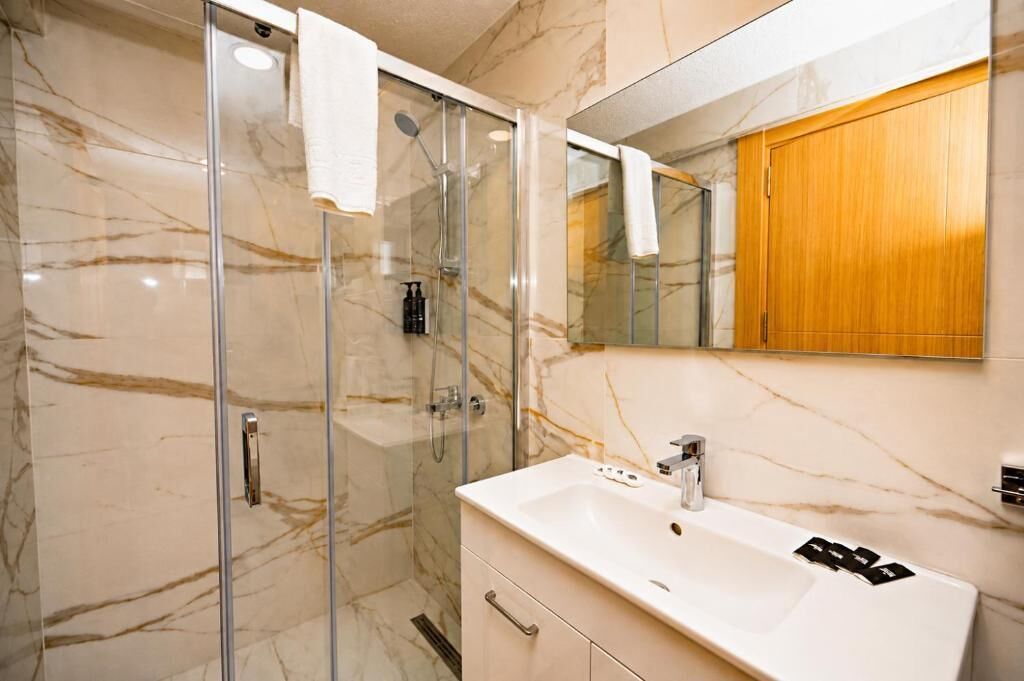 Une salle de bain avec une douche à parois de verre, un lavabo blanc et un meuble en bois.